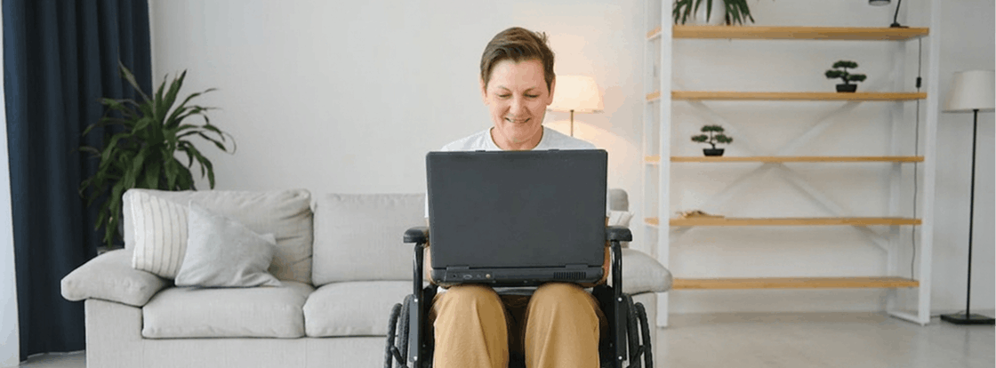 Person in wheelchair using laptop in living room.