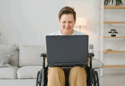 Person in wheelchair using laptop in living room.