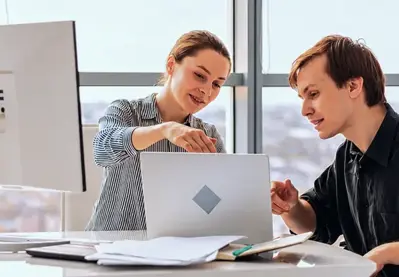 Two colleagues collaborating on a laptop in an office.